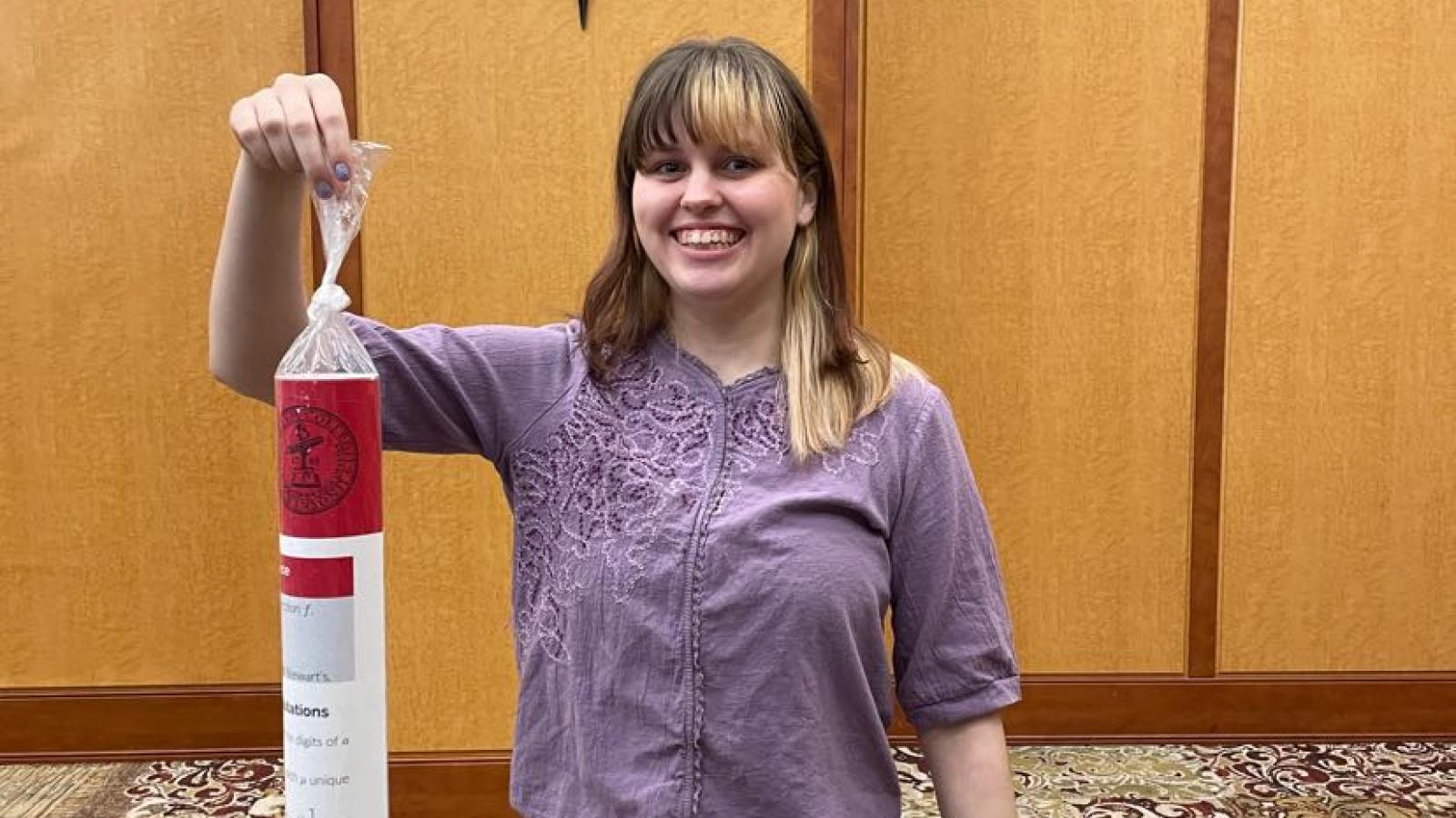 Megan holds her honors thesis poster like a man holds a prize fish